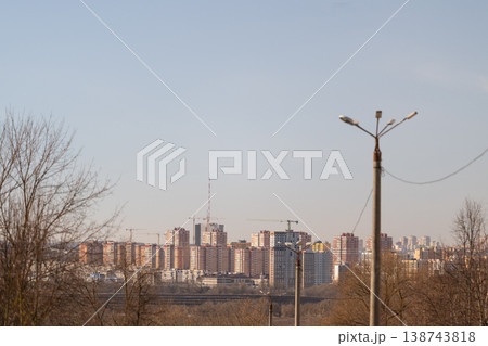 Cityscape with illuminated buildings. Modern city outline with early spring natural surroundings. Skyline of contemporary cityscape visible through leafless trees at dawn Cityscape with illuminated buildings. Modern city outline with early spring natural surroundings. Skyline of contemporary cityscape visible through leafless trees at dawn 138743818