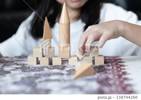 Small hands rebuild a wooden block tower on a soft rug placing pieces back with care after movement to fix and stabilize the structure. Small hands rebuild a wooden block tower on a soft rug placing pieces back with care after movement to fix and stabilize the structure. 138744260