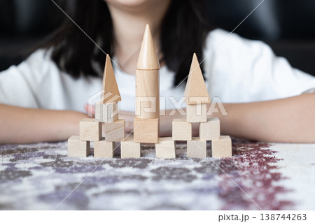A child places wooden pieces with steady hands to complete the tower. The simple build suggests confidence, progress and self trust. A child places wooden pieces with steady hands to complete the tower. The simple build suggests confidence, progress and self trust. 138744263
