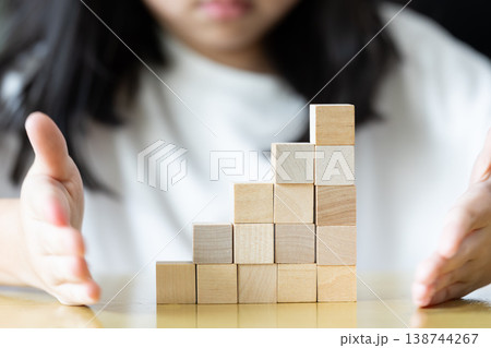 oth hands hold a wooden block tower as small fingers slowly adjust and place pieces one by one on a rug keeping the structure upright neat and stable through careful practice. 138744267