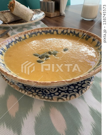 Creamy pumpkin soup in decorative bowl on patterned tablecloth background Creamy pumpkin soup in decorative bowl on patterned tablecloth background 138745573