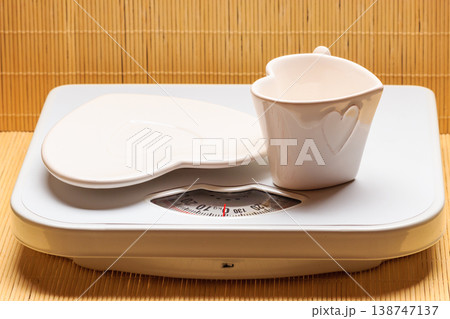 Empty plate saucer and mug cup on weighing scale. Empty plate saucer and mug cup on weighing scale. 138747137