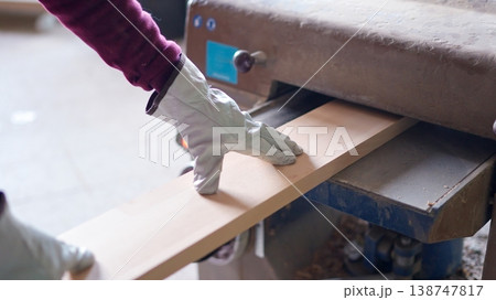 Worker planing wood plank using thickness planer in workshop 138747817