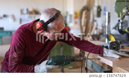 Carpenter drilling wood plank wearing safety equipment Carpenter drilling wood plank wearing safety equipment 138747829