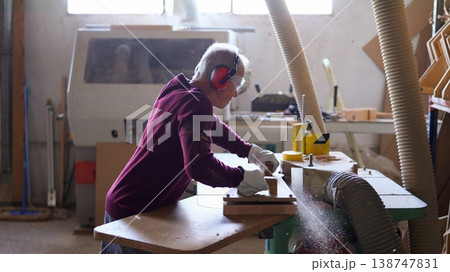 Woodworker shaping wood piece using wood shaper in workshop Woodworker shaping wood piece using wood shaper in workshop 138747831