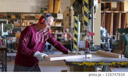 Carpenter cutting wood on a bandsaw in workshop 138747838