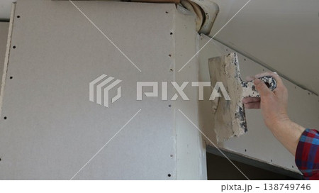 A spatula in the hand of a person repairing a room wall under the ceiling near a rounded corner and a doorway, filling holes during the installation of a room partition 138749746
