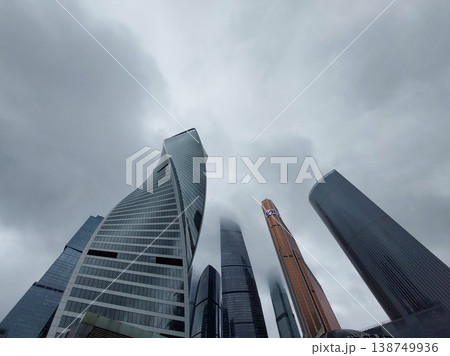 Low-angle view of high-rise city buildings under gray clouds Low-angle view of high-rise city buildings under gray clouds 138749936