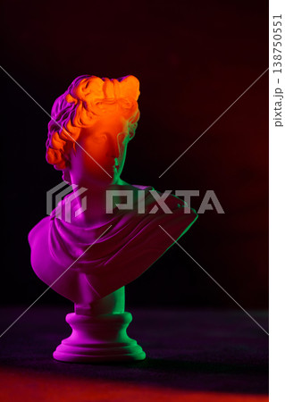 Classical bust sculpture illuminated with vibrant neon orange purple and green lighting effects Classical bust sculpture illuminated with vibrant neon orange purple and green lighting effects 138750551