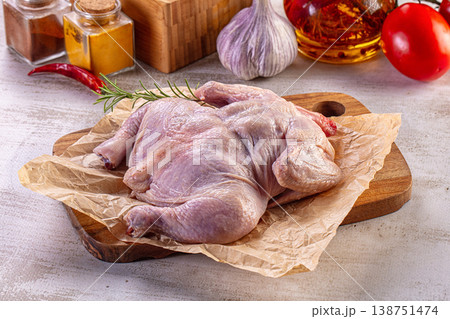 Raw spatchcock chicken on a cutting board surrounded by fresh spices and vegetables for cooking. Raw spatchcock chicken on a cutting board surrounded by fresh spices and vegetables for cooking. 138751474