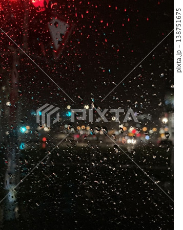 Raindrops on a car windshield at night with blurred city lights outside, capturing rainy urban ambiance, reflections, and moody nighttime atmosphere. 138751675
