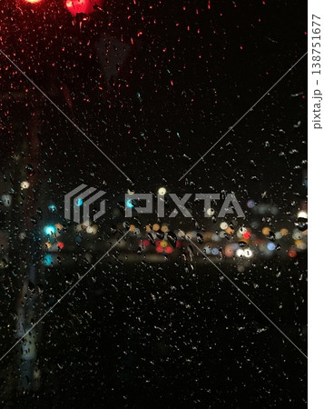 Raindrops on a car windshield at night with blurred city lights outside, capturing rainy urban ambiance, reflections, and moody nighttime atmosphere. 138751677