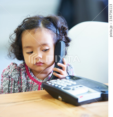Listening, talking and a child on a telephone phone call for communication in a house. Home, contact and a girl, kid or baby speaking on a landline for conversation, play or a discussion at a desk 138756113