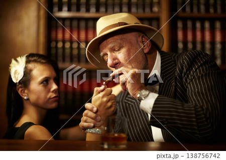 Mafia, boss and man with cigarette in office, woman and light for smoking. Mature person, godfather and hat in suit for power, reputation and career for criminal activity with tobacco for relaxation Mafia, boss and man with cigarette in office, woman and light for smoking. Mature person, godfather and hat in suit for power, reputation and career for criminal activity with tobacco for relaxation 138756742