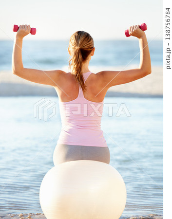 Woman, pilates ball and sitting with dumbbell for fitness on beach, fresh air or peace. Female instructor, stretching or balance in back view for health, wellness or zen for meditation for outdoors Woman, pilates ball and sitting with dumbbell for fitness on beach, fresh air or peace. Female instructor, stretching or balance in back view for health, wellness or zen for meditation for outdoors 138756784