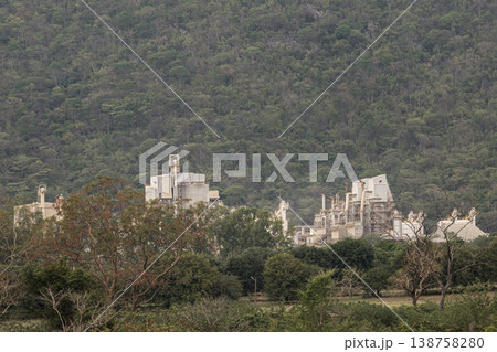 a vast industrial complex nestled at the base of a densely forested mountain, illustrating the intersection of heavy industry and the natural environment. 138758280