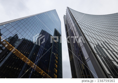 Looking up at towering glass office buildings against a cloudy sky Looking up at towering glass office buildings against a cloudy sky 138759161