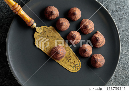 Chocolate truffles and vintage brass cake server on a black plate. Chocolate truffles and vintage brass cake server on a black plate. 138759343