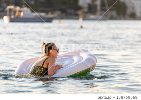 Woman wear green swimsuit relax inflatable ring calm sea near yachts forested coast sunset warm summer sunlight. Female person peaceful moment  leisure freedom vacation lifestyle serene getaway mood 138759369