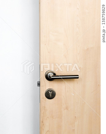 Wooden door in room, surface with smooth finish. Metal handle, keyhole for locking. Simple design against plain wall. Natural light illuminates room, interior, closeup 138759829