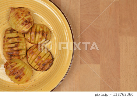 Baked hasselback potatoes on a yellow plate 138762360