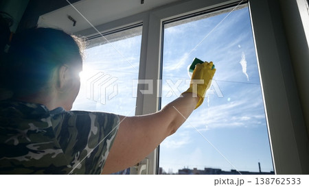 Woman cleans window on sunny day in urban setting while wearing gloves 138762533
