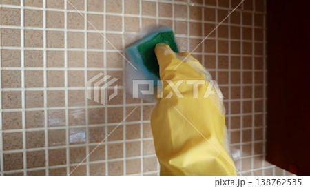 Scrubbing tiles with a sponge covered in soap inside a kitchen Scrubbing tiles with a sponge covered in soap inside a kitchen 138762535
