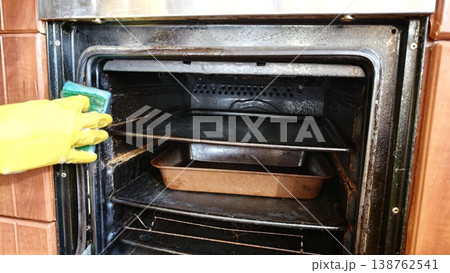 Cleaning an oven with a sponge while wearing rubber gloves in a kitchen 138762541