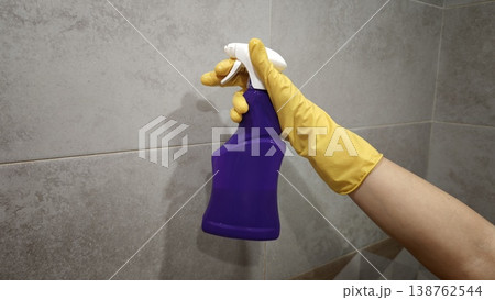 Person holding a purple cleaning spray bottle in a bathroom setting at home Person holding a purple cleaning spray bottle in a bathroom setting at home 138762544