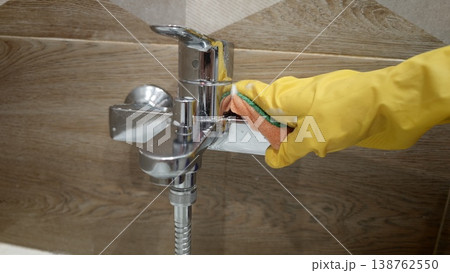 Cleaning a shiny faucet in a bathroom with a sponge and rubber glove Cleaning a shiny faucet in a bathroom with a sponge and rubber glove 138762550