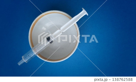 Syringe placed on a white bowl against a blue background during a health activity Syringe placed on a white bowl against a blue background during a health activity 138762588