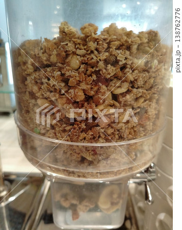 Granola dispenser filled with mixed granola ingredients including oats, nuts, and seeds, positioned in a buffet-style setting for breakfast options 138762776