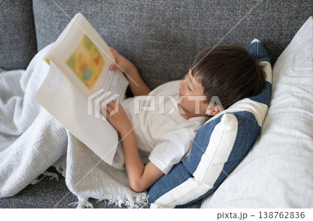 Boy Enjoys Reading a Colorful Storybook at Home on a Cozy Sofa Boy Enjoys Reading a Colorful Storybook at Home on a Cozy Sofa 138762836