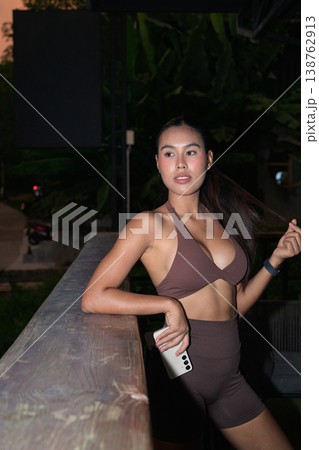 Athletic Thai Woman in Brown Yoga Set Leaning on Balcony Railing Healthy Lifestyle Concept 138762913