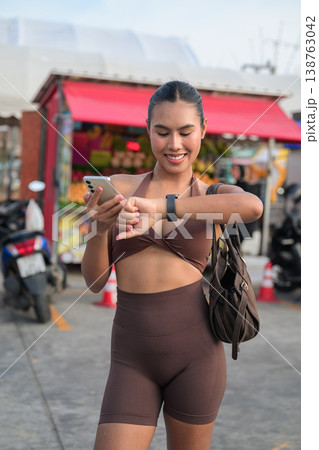 Thai Fitness Influencer Checking Smartwatch at Tropical Outdoor Market Modern Digital Lifestyle Concept Thai Fitness Influencer Checking Smartwatch at Tropical Outdoor Market Modern Digital Lifestyle Concept 138763042