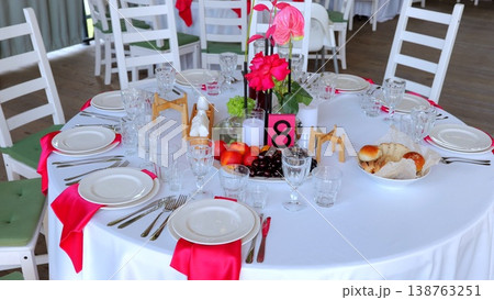 Elegant banquet table covered with crisp white linen, adorned with blush rose and anthurium centerpiece, displaying numbered marker eight, ready for upcoming celebration Elegant banquet table covered with crisp white linen, adorned with blush rose and anthurium centerpiece, displaying numbered marker eight, ready for upcoming celebration 138763251