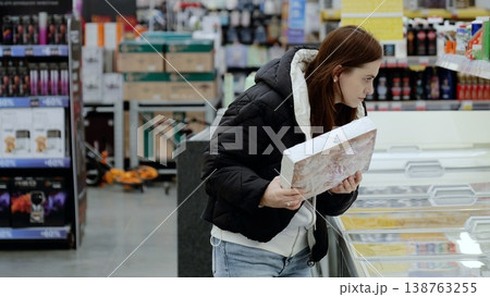 Woman shopping for groceries, choosing frozen food in brightly lit supermarket 138763255