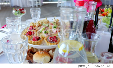 Elegant miniature tarts and canapes adorning reception table, complementing beverages with refined culinary presentation for wedding celebration Elegant miniature tarts and canapes adorning reception table, complementing beverages with refined culinary presentation for wedding celebration 138763258