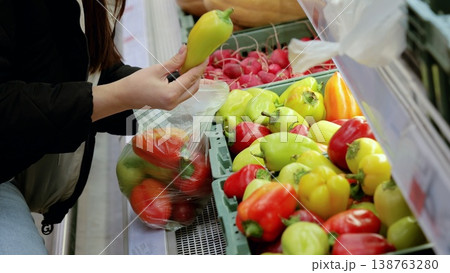 Customer picking out fresh bell peppers from a grocery store display, holding a bag filled with vibrant vegetables Customer picking out fresh bell peppers from a grocery store display, holding a bag filled with vibrant vegetables 138763280