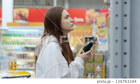 Young woman carefully selecting soy sauce at a supermarket, making informed choices about food products by reading the label on the bottle 138763284