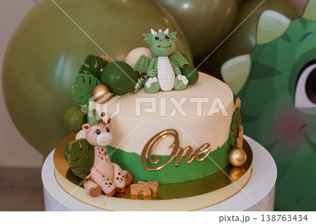 First birthday cake with green dragon and giraffe toppers, gold lettering, jungle theme, fondant decoration on white stand First birthday cake with green dragon and giraffe toppers, gold lettering, jungle theme, fondant decoration on white stand 138763434