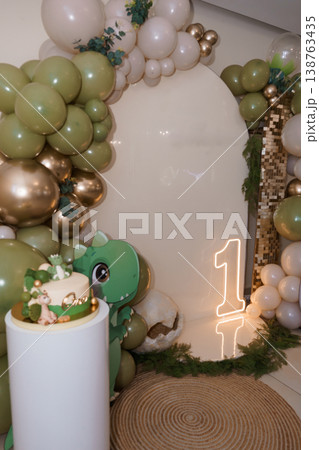 First birthday party setup with green dinosaur cake and balloon arch decoration featuring gold and sage green accents with neon number one sign First birthday party setup with green dinosaur cake and balloon arch decoration featuring gold and sage green accents with neon number one sign 138763435
