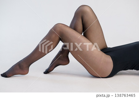 Close up of woman legs in black sheer tights lying on white floor in minimalist studio setting. Close up of woman legs in black sheer tights lying on white floor in minimalist studio setting. 138763465