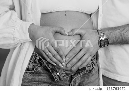 Pregnant woman and partner making heart shape with hands on belly in black and white photography 138763472