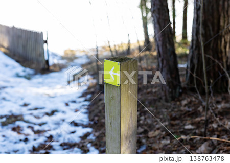 Snowy trail sign points left. Calm scene with snow melting and nature inviting exploration Snowy trail sign points left. Calm scene with snow melting and nature inviting exploration 138763478