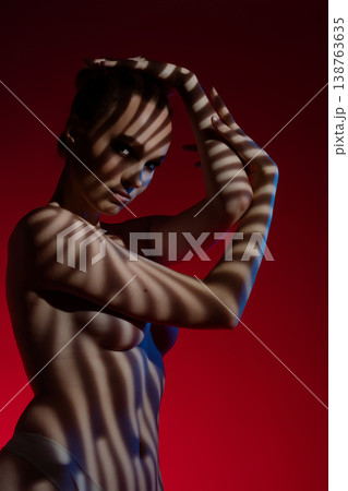 Woman poses gracefully against a red background with striking shadows at night Woman poses gracefully against a red background with striking shadows at night 138763635
