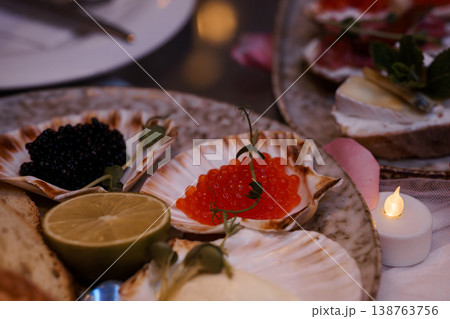 Gourmet caviar and salmon roe served on seashell plates with lemon, bread, and candlelight for luxury dining. 138763756