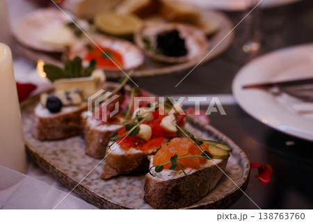 Gourmet salmon and cheese bruschetta on rustic ceramic platter with candles and blurred background. Gourmet salmon and cheese bruschetta on rustic ceramic platter with candles and blurred background. 138763760