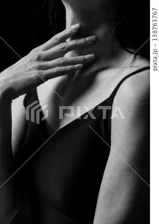 Black and white portrait of woman touching neck with manicured nails in dark studio lighting 138763767