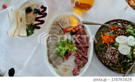 Sliced roast beef, meatloaf, pate, and a salad with boiled eggs are beautifully arranged on plates, creating an elegant and appetizing table setting for a celebratory meal Sliced roast beef, meatloaf, pate, and a salad with boiled eggs are beautifully arranged on plates, creating an elegant and appetizing table setting for a celebratory meal 138763829